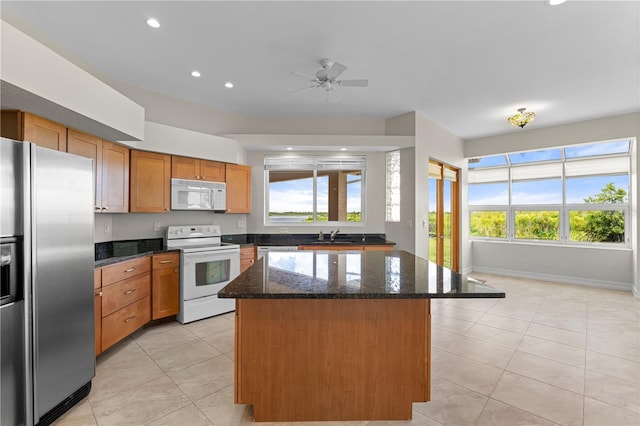 kitchen featuring ceiling fan, a kitchen island, dark stone countertops, and white appliances