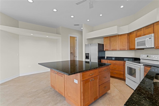 kitchen featuring white appliances, ceiling fan, light tile patterned floors, dark stone countertops, and a center island