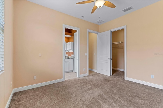 unfurnished bedroom with ensuite bath, ceiling fan, a walk in closet, light carpet, and a closet