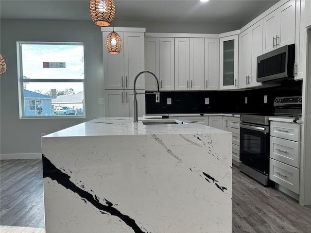 kitchen featuring hanging light fixtures, decorative backsplash, light wood-type flooring, light stone counters, and stainless steel appliances