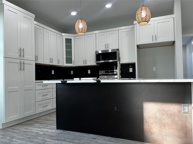 kitchen featuring stove, light wood-type flooring, tasteful backsplash, white cabinets, and hanging light fixtures