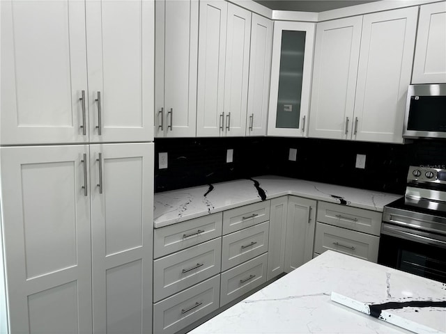 kitchen with light stone countertops, appliances with stainless steel finishes, white cabinets, and decorative backsplash