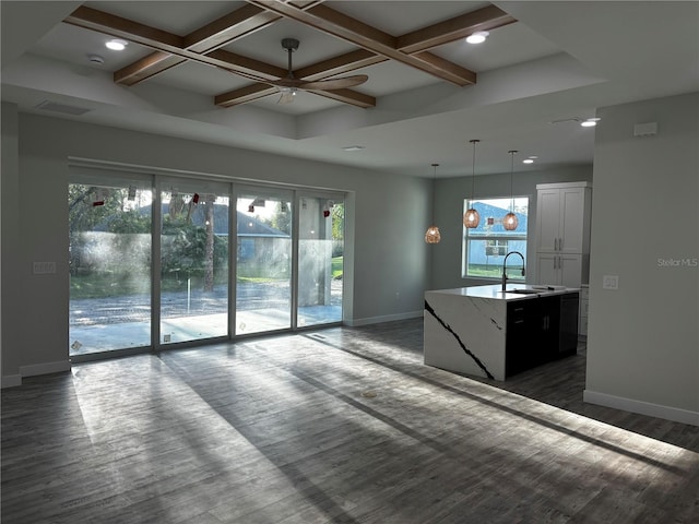 kitchen featuring coffered ceiling, a center island with sink, white cabinets, sink, and decorative light fixtures