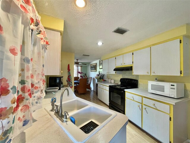 kitchen with light hardwood / wood-style floors, ceiling fan, electric range, sink, and a textured ceiling