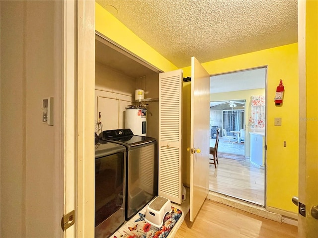 laundry room featuring washer and clothes dryer, light hardwood / wood-style floors, a textured ceiling, and electric water heater