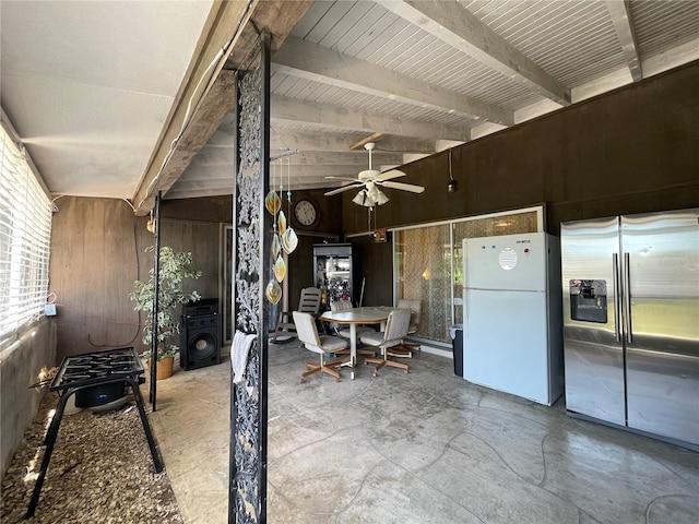 interior space featuring white refrigerator, stainless steel refrigerator with ice dispenser, wood walls, ceiling fan, and concrete flooring