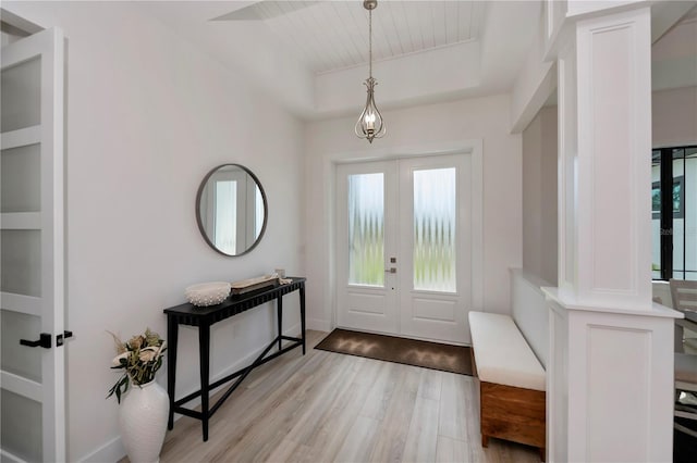 foyer featuring a tray ceiling, french doors, ornate columns, and light hardwood / wood-style flooring