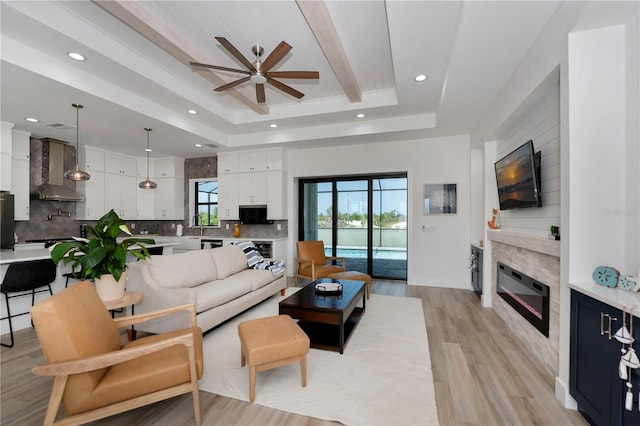 living room with ceiling fan, a raised ceiling, light hardwood / wood-style flooring, and sink