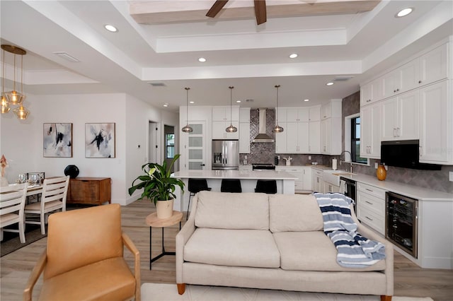 living room with ceiling fan, a tray ceiling, wine cooler, light wood-type flooring, and sink