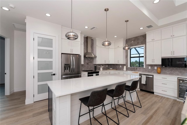 kitchen featuring light hardwood / wood-style flooring, pendant lighting, a center island, wall chimney exhaust hood, and appliances with stainless steel finishes