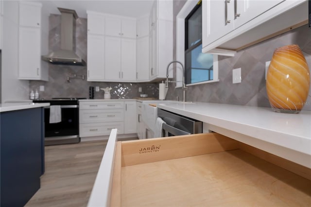 kitchen featuring light hardwood / wood-style floors, white cabinetry, range, wall chimney exhaust hood, and backsplash