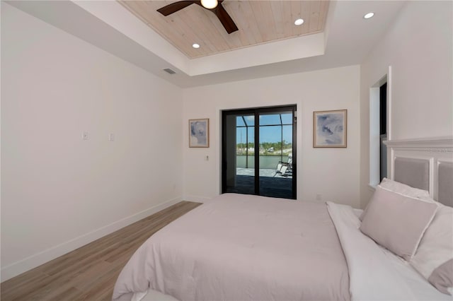 bedroom with a water view, access to exterior, ceiling fan, a tray ceiling, and hardwood / wood-style floors