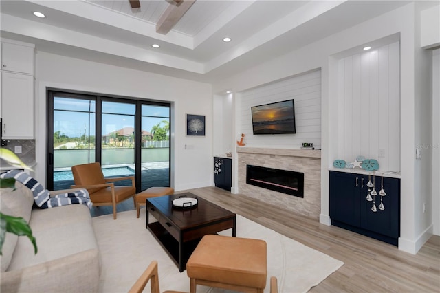 living room with ceiling fan, a tray ceiling, and light wood-type flooring