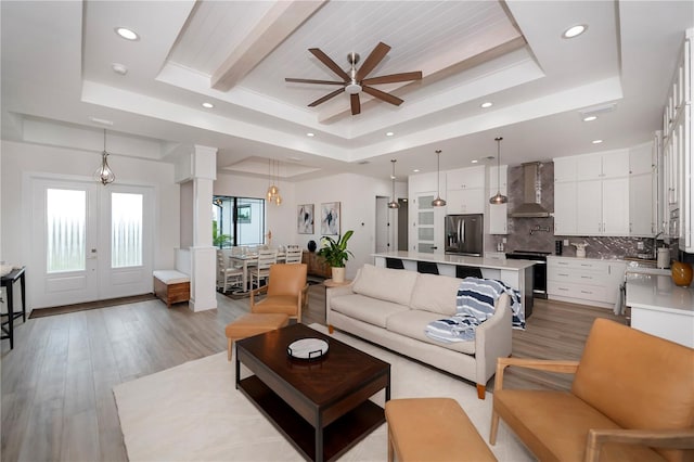 living room with a wealth of natural light, light hardwood / wood-style floors, ceiling fan, and a tray ceiling