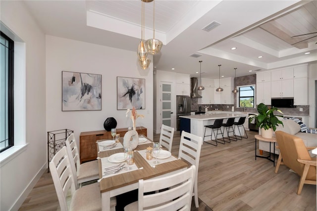 dining area with sink, light hardwood / wood-style flooring, and a raised ceiling