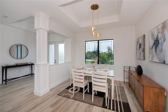 dining space with a raised ceiling, light hardwood / wood-style floors, a chandelier, and ornate columns