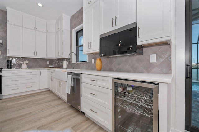 kitchen with beverage cooler, light hardwood / wood-style flooring, tasteful backsplash, stainless steel dishwasher, and white cabinetry