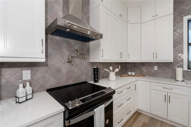 kitchen with wall chimney range hood, tasteful backsplash, light wood-type flooring, stainless steel range with electric cooktop, and white cabinets