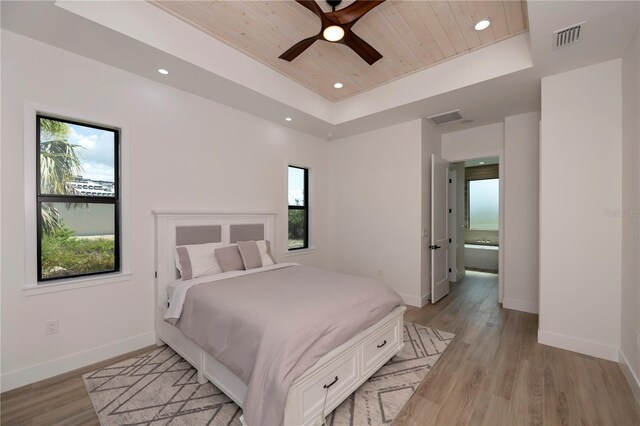 bedroom featuring multiple windows, a tray ceiling, light wood-type flooring, and ceiling fan