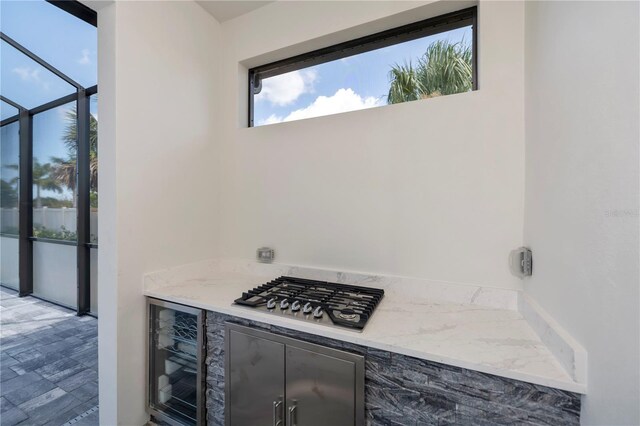 kitchen with beverage cooler, stainless steel gas stovetop, and light stone counters