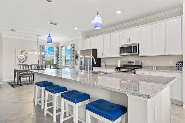 kitchen with white cabinets, hanging light fixtures, a kitchen island with sink, and appliances with stainless steel finishes