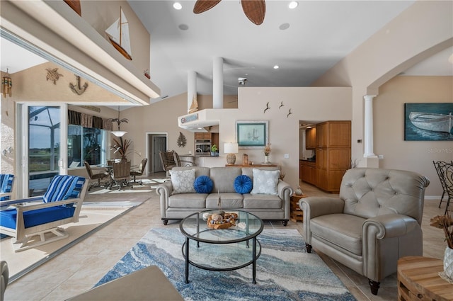 tiled living room with ceiling fan, ornate columns, and high vaulted ceiling