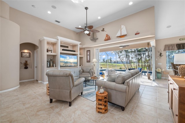 living room featuring ceiling fan, built in shelves, a towering ceiling, and light tile patterned flooring