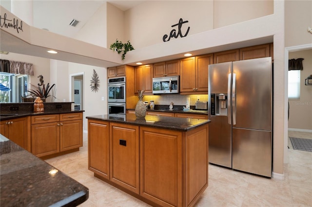 kitchen featuring appliances with stainless steel finishes, tasteful backsplash, a high ceiling, dark stone counters, and a kitchen island