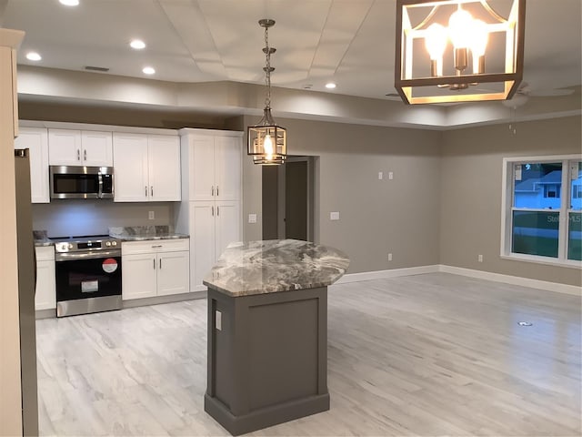 kitchen featuring appliances with stainless steel finishes, decorative light fixtures, white cabinets, a center island, and light stone countertops