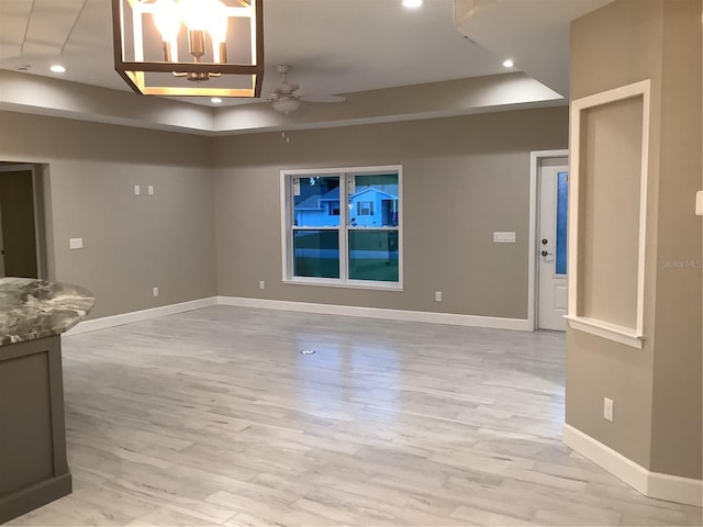 unfurnished living room with ceiling fan, a raised ceiling, and light hardwood / wood-style flooring