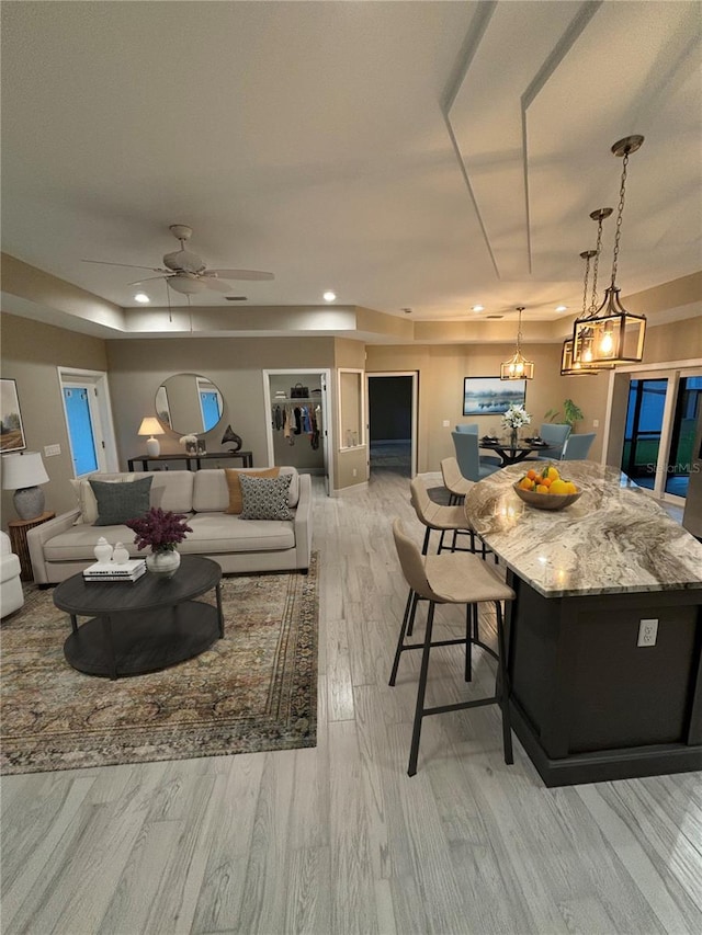 living room featuring ceiling fan with notable chandelier, light wood-type flooring, and a tray ceiling