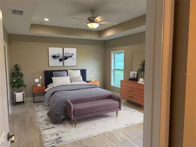 bedroom with ceiling fan, a raised ceiling, and light hardwood / wood-style floors