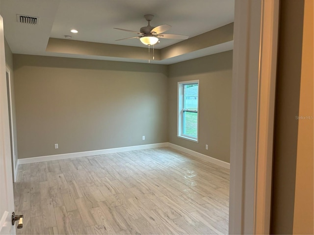 unfurnished room featuring a raised ceiling, ceiling fan, and light hardwood / wood-style floors