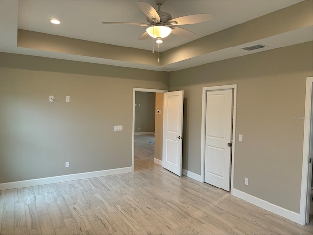 unfurnished bedroom featuring ceiling fan, a tray ceiling, and light hardwood / wood-style flooring