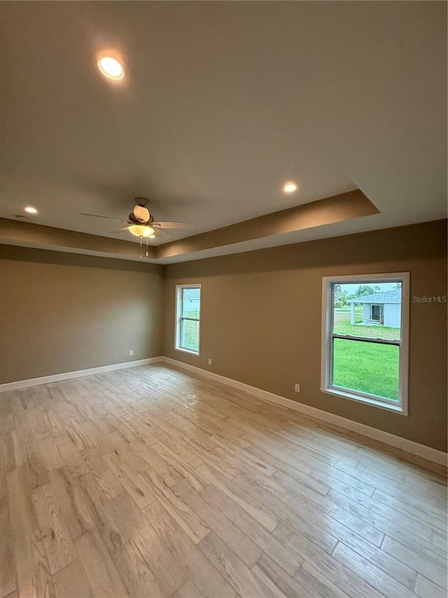 empty room with a raised ceiling, ceiling fan, and light wood-type flooring