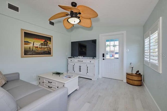 living room featuring light hardwood / wood-style flooring, ceiling fan, and a healthy amount of sunlight