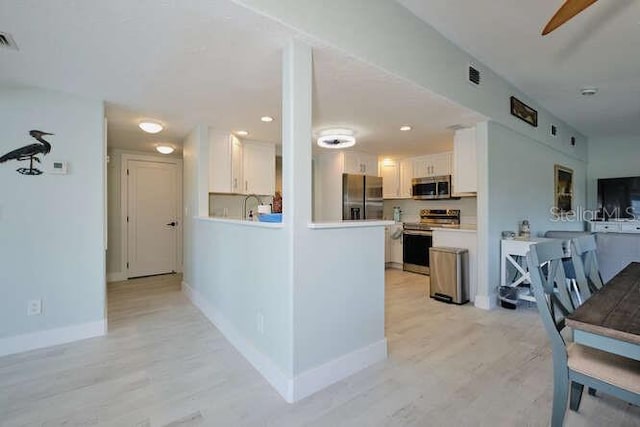 kitchen featuring white cabinets, light wood-type flooring, stainless steel appliances, and ceiling fan