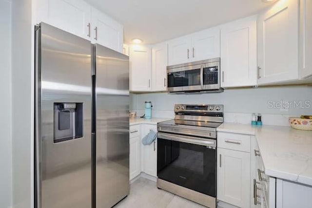 kitchen with white cabinets, appliances with stainless steel finishes, and light stone counters