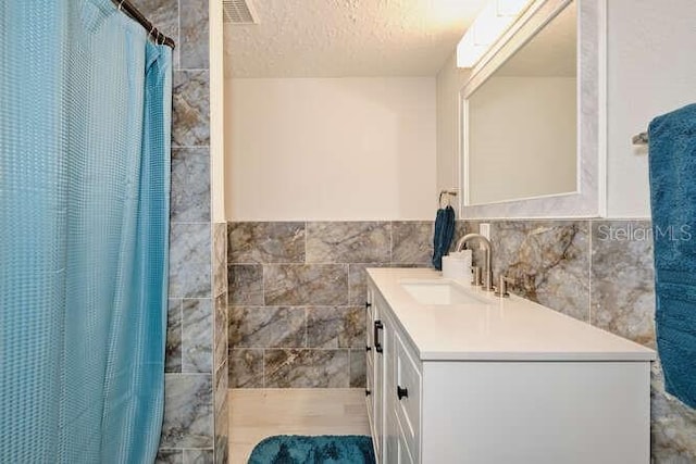 bathroom featuring a shower with curtain, vanity, tile walls, and a textured ceiling