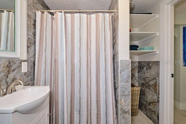 bathroom featuring tile walls, curtained shower, vanity, and a textured ceiling