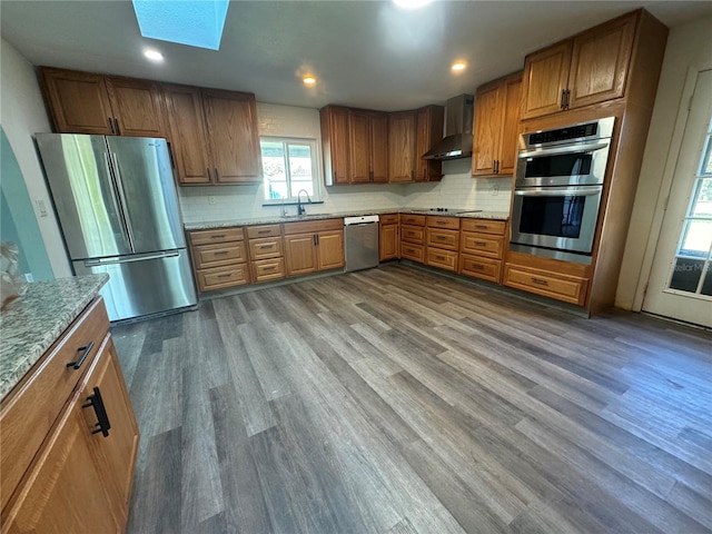 kitchen with wall chimney exhaust hood, stainless steel appliances, sink, and hardwood / wood-style floors