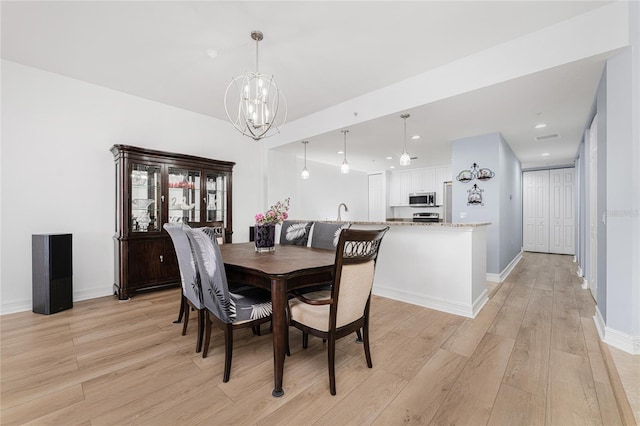 dining area with sink, an inviting chandelier, and light wood-type flooring