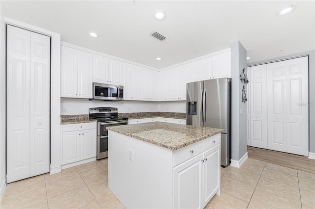 kitchen featuring a center island, light tile patterned floors, appliances with stainless steel finishes, light stone counters, and white cabinetry