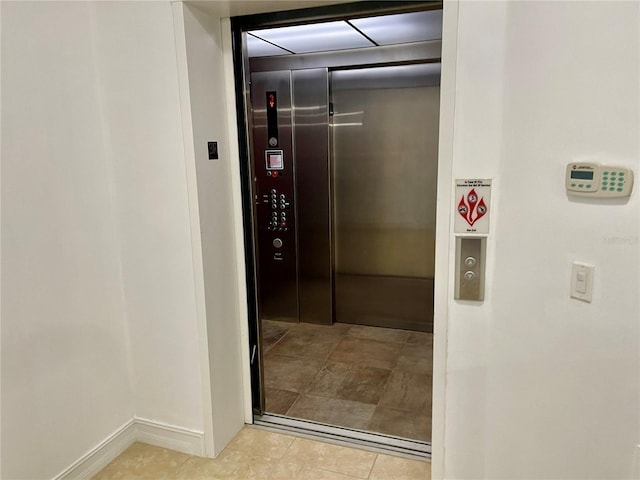 hall with elevator, baseboards, and light tile patterned floors