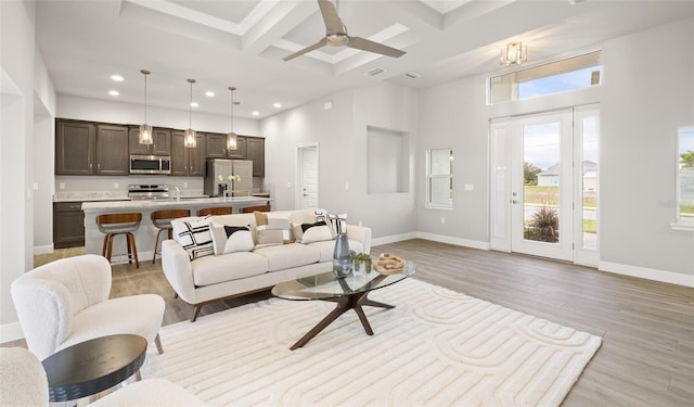 living room with coffered ceiling, ceiling fan, beam ceiling, light hardwood / wood-style flooring, and a high ceiling