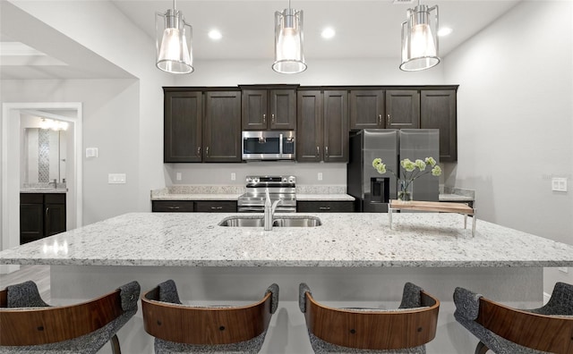 kitchen with dark brown cabinetry, stainless steel appliances, sink, decorative light fixtures, and an island with sink