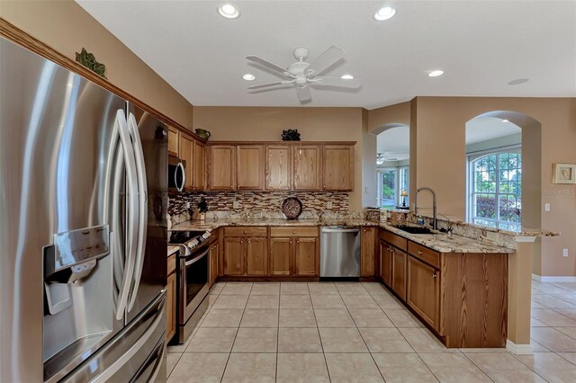 kitchen featuring appliances with stainless steel finishes, sink, backsplash, kitchen peninsula, and light stone countertops