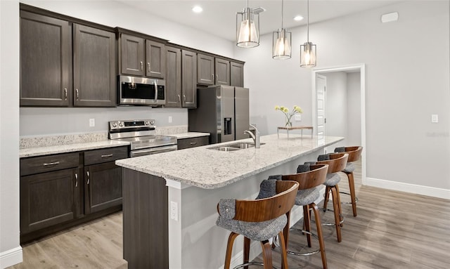 kitchen featuring sink, stainless steel appliances, decorative light fixtures, a kitchen bar, and a center island with sink