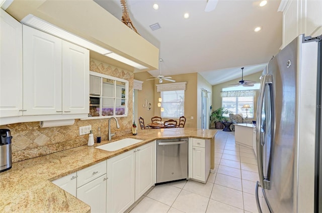 kitchen featuring kitchen peninsula, light stone countertops, stainless steel appliances, vaulted ceiling, and white cabinets