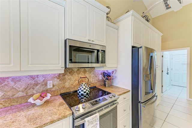 kitchen with tasteful backsplash, white cabinets, light tile patterned floors, and appliances with stainless steel finishes